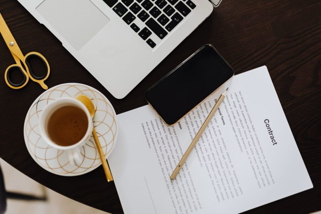 Draufsicht auf einen Schreibtisch mit Vertrag, Laptop, Smartphone und Kaffeetasse